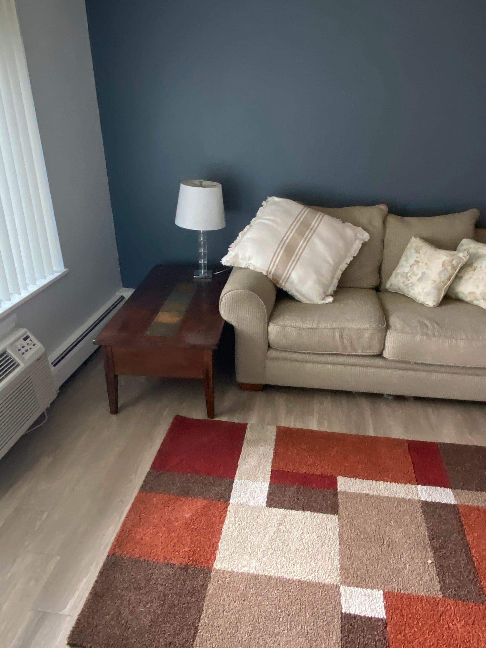 A furnished living room with a beige sofa, a wooden coffee table, a lamp and a patterned rug
